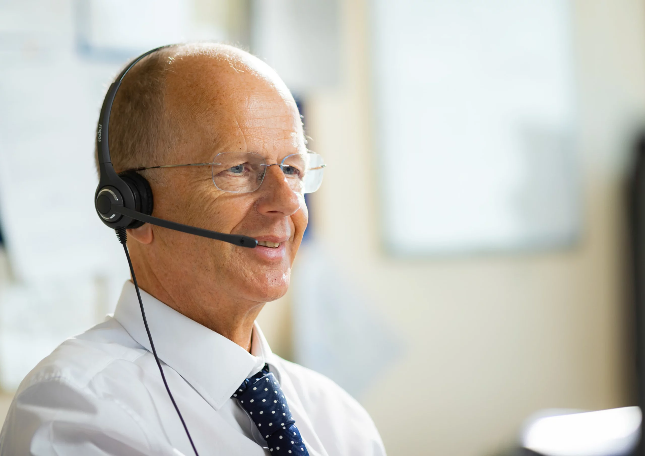 NHS Kent & Medway - Smartly dressed man with headset on and glasses smiling